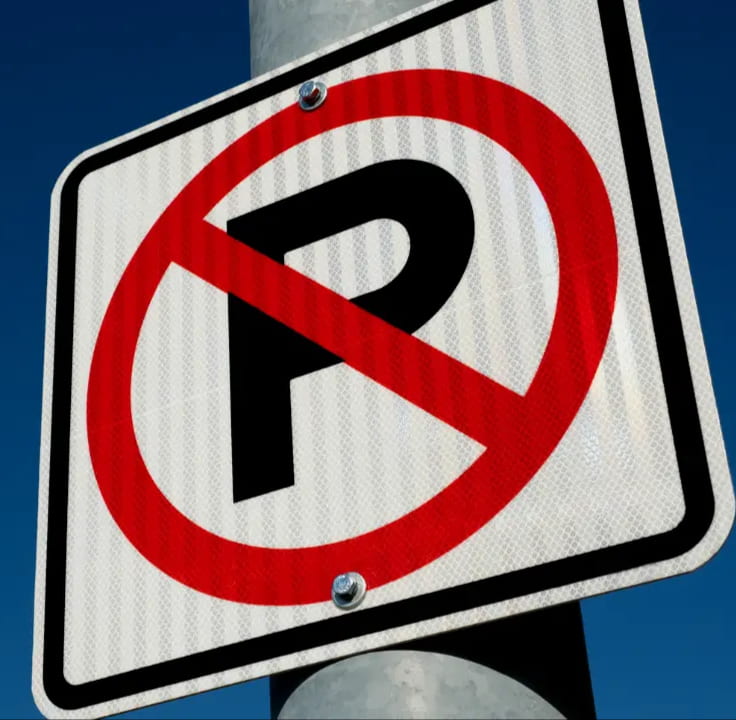 No parking sign with a black letter P crossed out by a red circle and diagonal line against a clear blue sky.