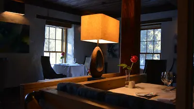 Cozy restaurant interior with a glowing table lamp and tables set with wine glasses and a single red rose in a vase.