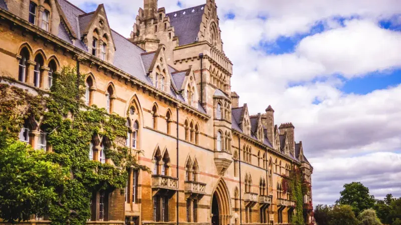 Historic stone building with Gothic architectural features and ivy on the walls under a partly cloudy sky.