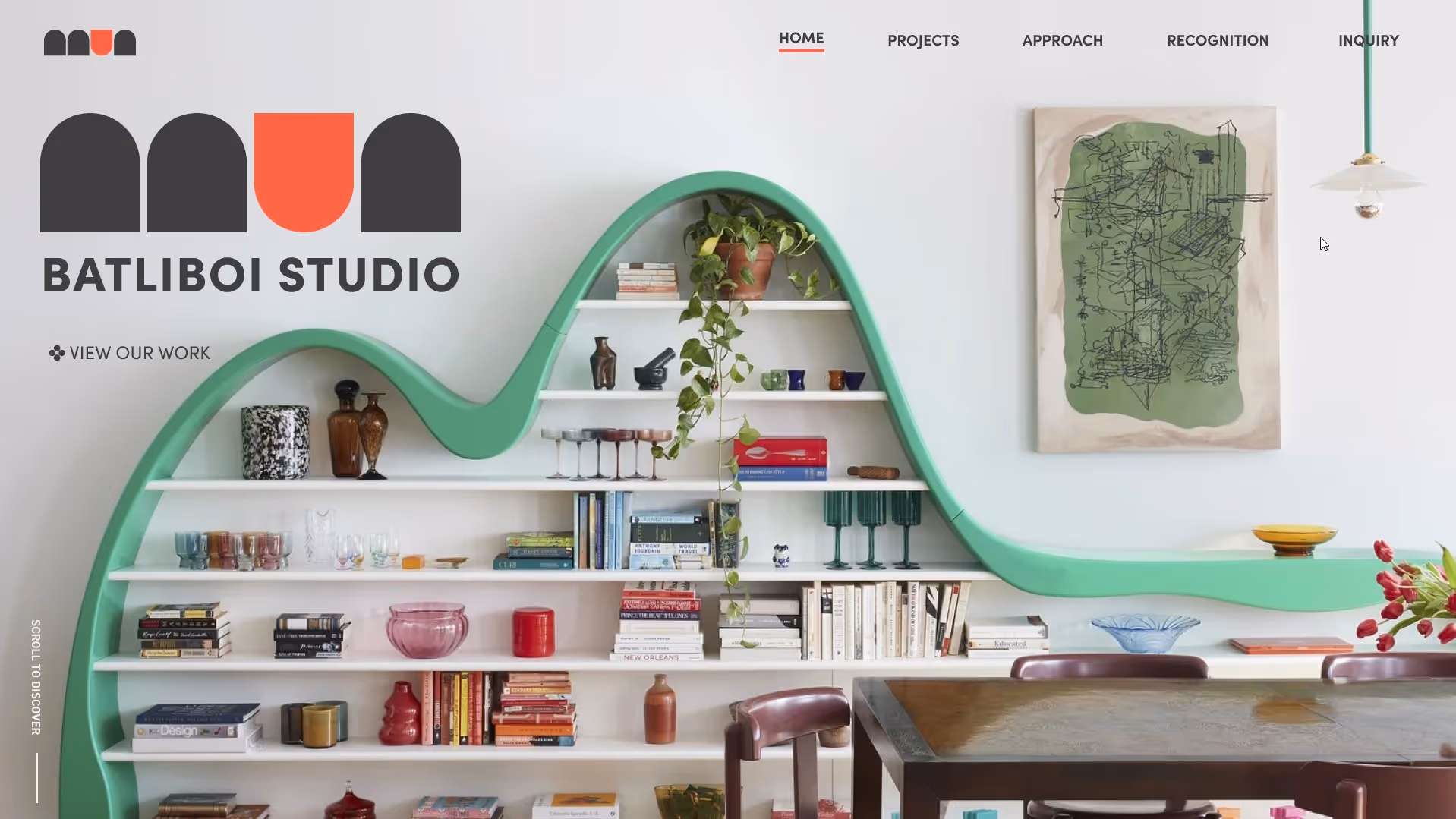 Modern interior with a green wave-shaped bookshelf filled with books and decorative items, a brown wooden table with chairs, a hanging white light, and abstract wall art.