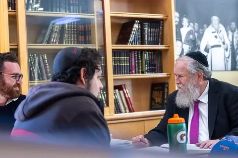 Young men learning at tables in the JETS beis midrash while a rabbi stands among them
