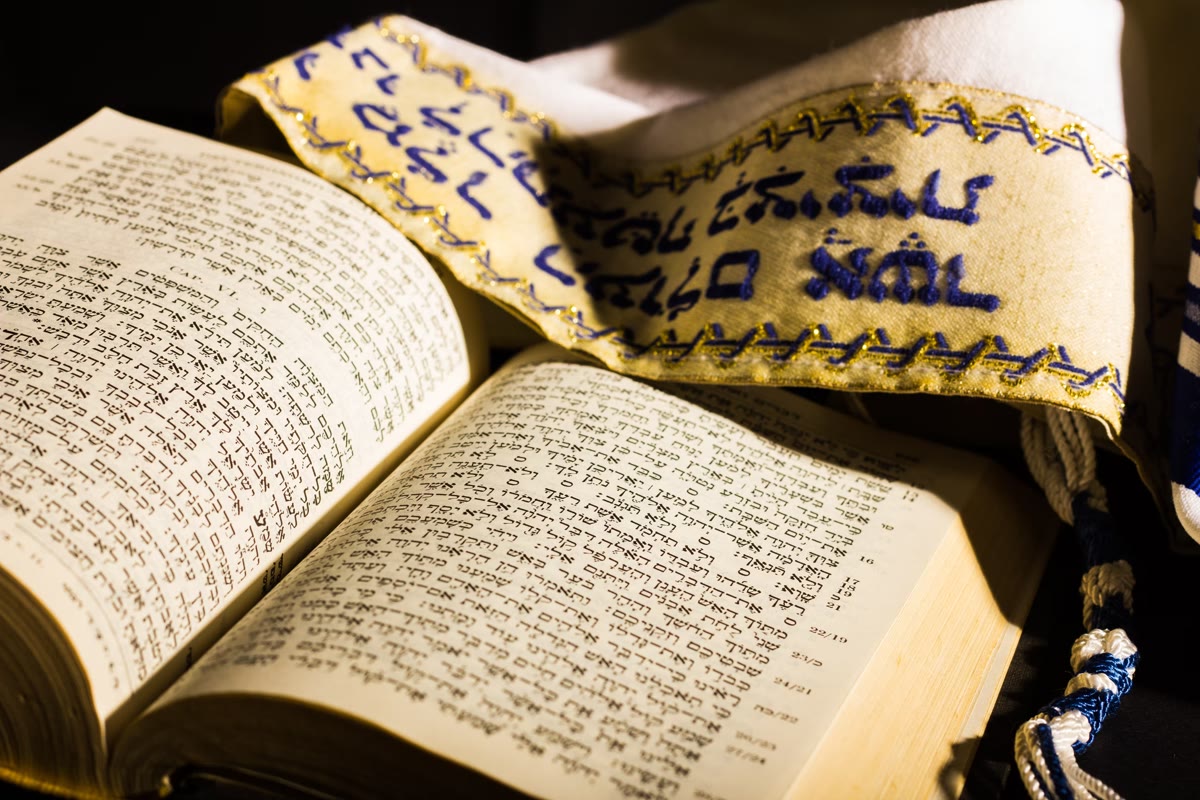 An open volume of Talmud with a tallit draped across it