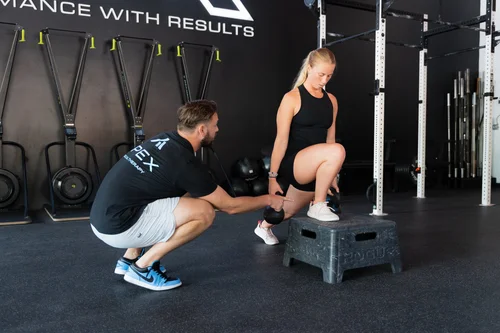 Physical therapist assists a woman stepping onto a workout box in a gym setting.