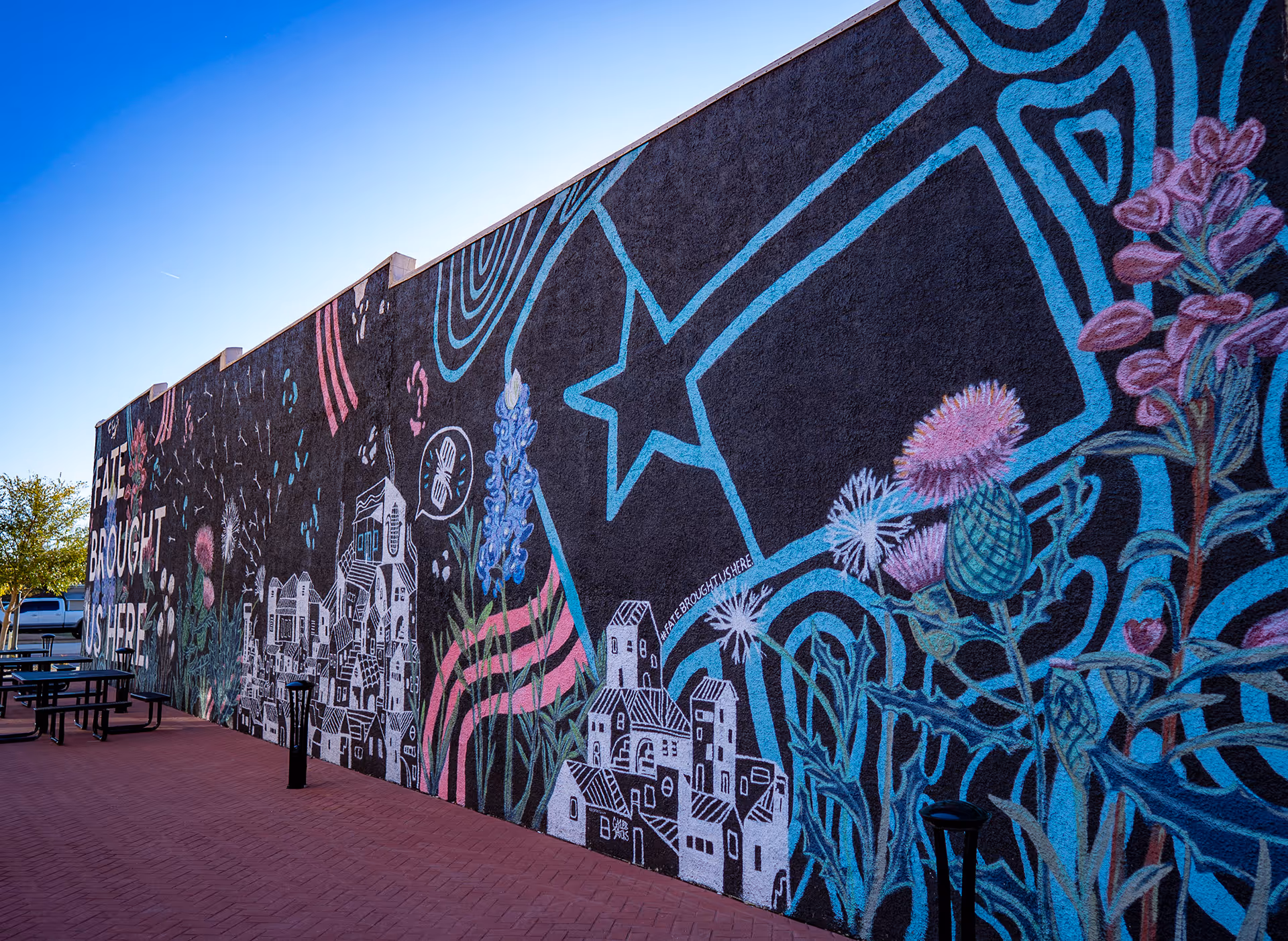 Colorful mural on a brick wall depicting flowers, houses, a large star, and the text 'FATE BROUGHT US HERE'.