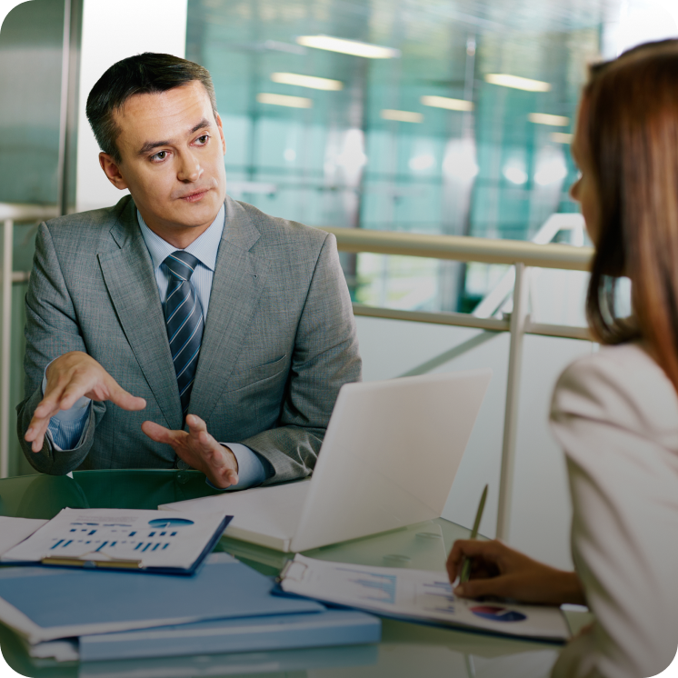 Businessman in gray suit explaining charts to a woman during a meeting in an office.