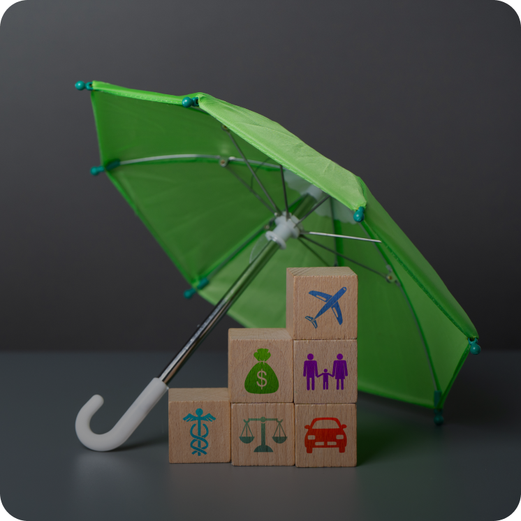 Green umbrella covering wooden blocks with icons representing health, justice, money, family, car, and airplane insurance.