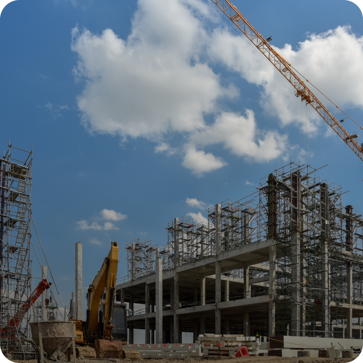 Construction site with concrete building framework, scaffolding, a yellow excavator, and a crane under a blue sky with scattered clouds.