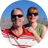 Man and woman wearing sunglasses posing outdoors with a desert mountain landscape in the background.