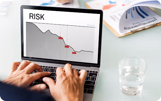 Person analyzing a declining risk graph on a laptop with documents and a glass of water on the desk.