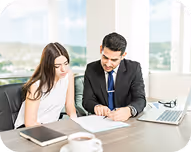 Businessman and businesswoman reviewing documents together at a table with laptop and coffee cup.