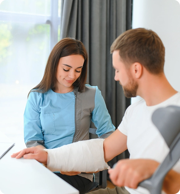Female healthcare professional in blue scrubs gently holding a man's casted arm in a medical setting.