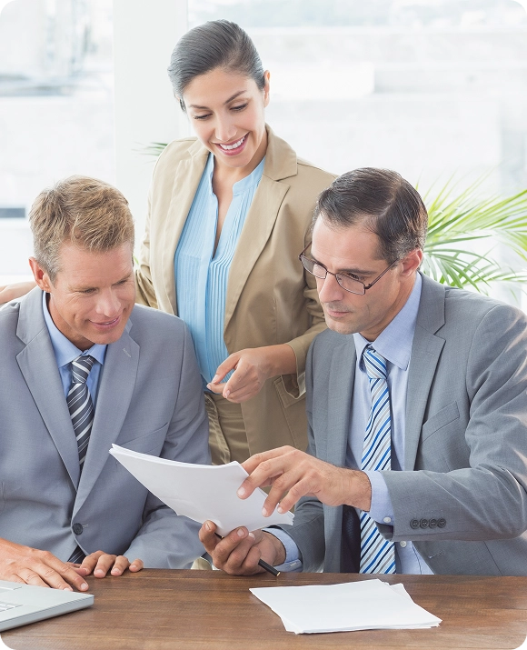 Three business professionals discussing documents at a table in a bright office.