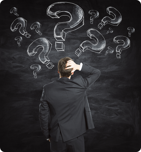 Man in suit scratching his head while looking at multiple large chalk-drawn question marks on a blackboard.