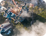 Aerial view of tall residential buildings surrounded by greenery and misty clouds.