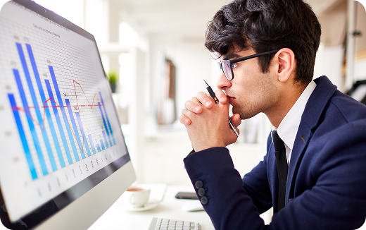 Man in a suit and glasses intently analyzing a computer screen displaying blue bar and red line graphs in an office.