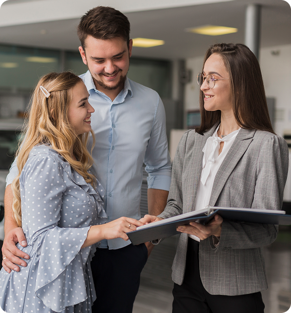 Businesswoman in glasses showing a folder to a smiling couple in a modern office.