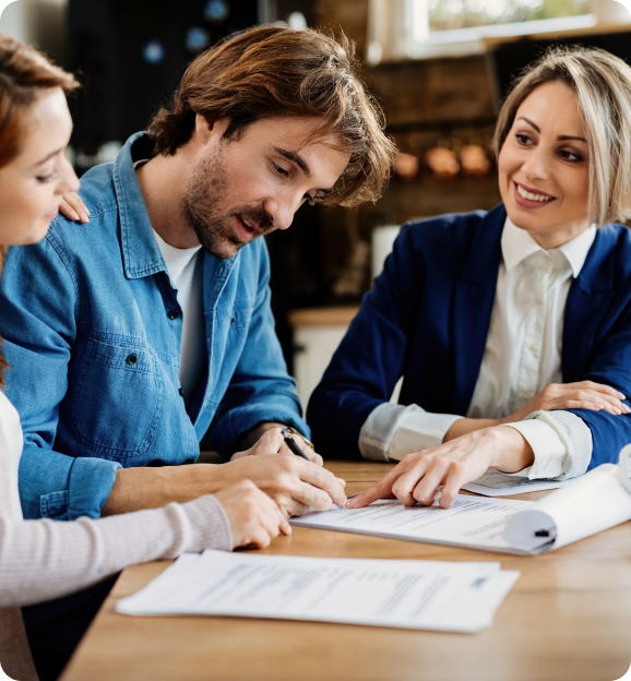 Man signing a document at a table while two women guide him through the paperwork.