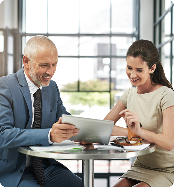 Smiling businessman and woman reviewing content on a tablet at a round table in a bright office.