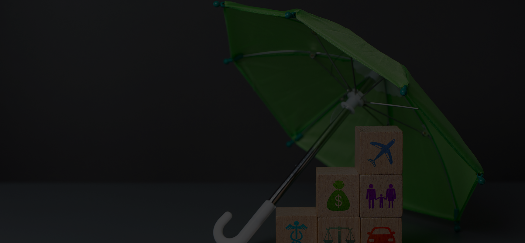 Green umbrella leaning to the right with wooden blocks stacked under it displaying icons for health, money, family, travel, and car insurance.
