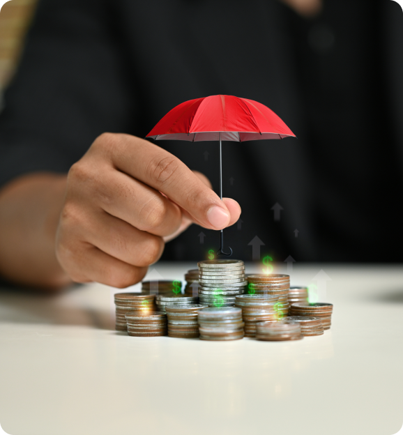 Hand holding a small red umbrella protecting stacks of coins symbolizing financial protection and insurance.