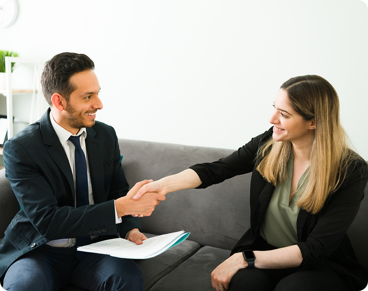 Smiling man and woman sitting on a couch shaking hands during a meeting.