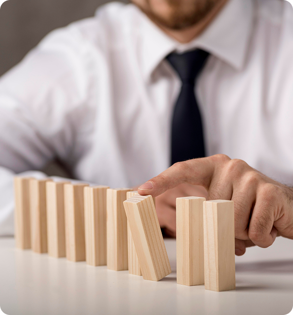 Man in white shirt and black tie stopping a row of falling wooden dominoes with his finger.