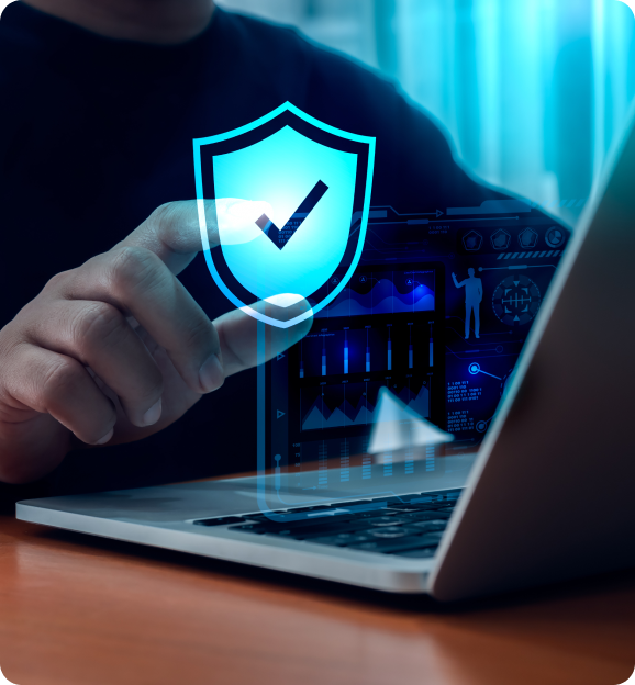 Close-up of a hand holding a digital shield with a checkmark icon hovering above a laptop keyboard, symbolizing cybersecurity protection.