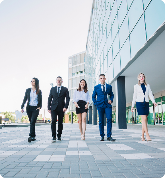 Diverse group of five business professionals confidently walking outdoors in front of a modern glass building.