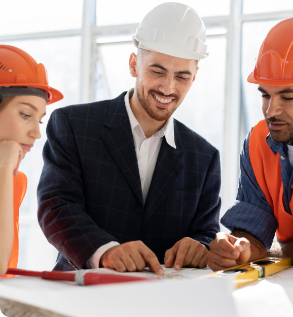 Three construction professionals, two wearing orange helmets and one in a white helmet and suit, reviewing building plans together.