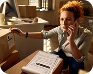 Woman on phone scanning a package with a barcode scanner in a sunlit room.
