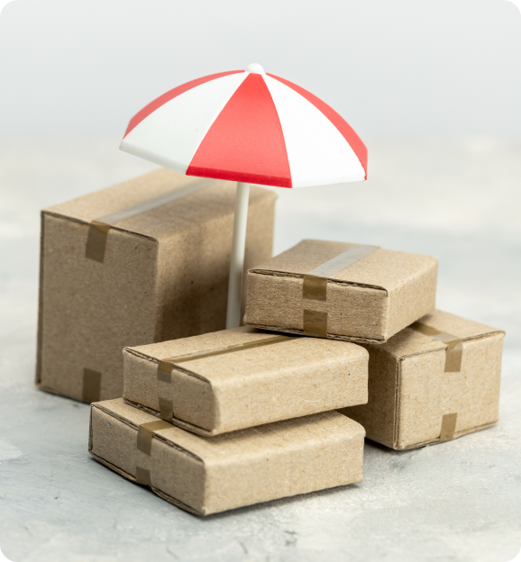 Stack of five cardboard boxes covered by a small red and white umbrella on a light surface.