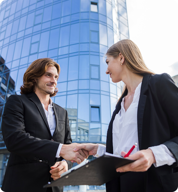 Two business professionals shaking hands outside a modern glass office building, one holding a clipboard and pen.