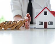 Person preventing wooden dominoes from falling in front of a small model house, symbolizing property damage protection.