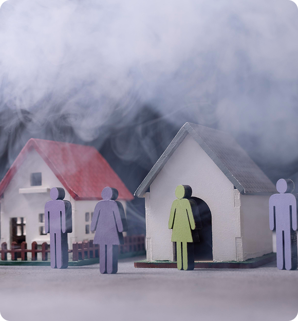 Miniature houses and colored paper cutout people surrounded by smoke symbolizing a natural disaster scenario.