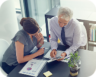 Two business professionals reviewing documents and charts together at an office desk.