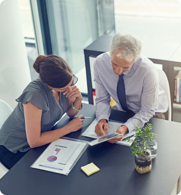 Two business professionals reviewing charts and data on papers and a tablet in a modern office.