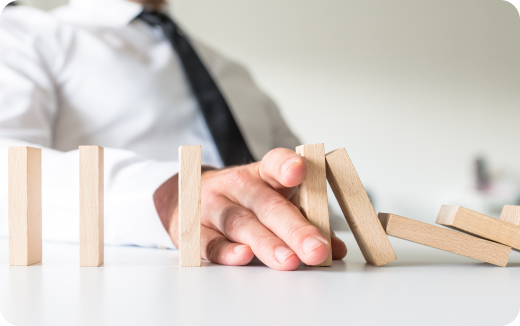 A person in a white shirt and black tie stops falling wooden dominoes with their hand on a table.