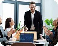 Business team applauding a smiling man standing at a conference table with a laptop in a modern office.