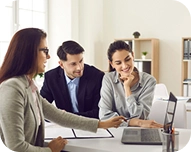 Three colleagues collaborating and discussing work around a laptop in a bright office.