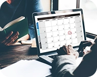 People working at a desk with a laptop displaying a digital calendar with a date circled in red.