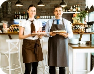 Two smiling bakery workers in aprons holding freshly baked bread in a cozy bakery.