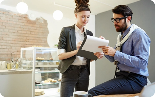 Two colleagues reviewing documents together in a modern cafe setting.