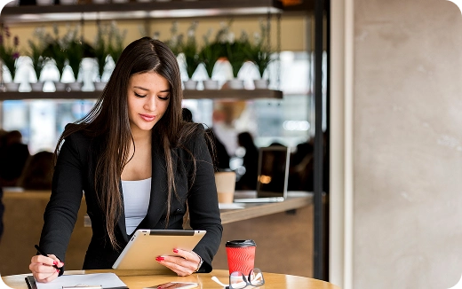 Young woman with long brown hair using a tablet while sitting at a wooden table with a cup of coffee in a modern café.