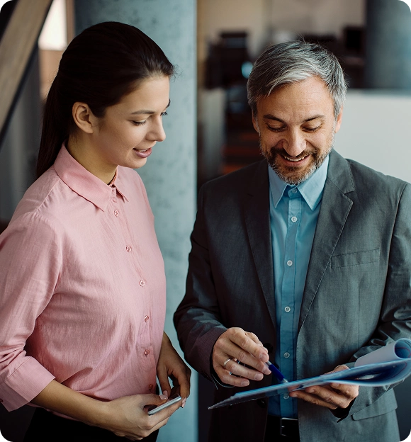 Smiling businesswoman and businessman reviewing documents together in an office setting.