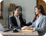 Two professional women in business attire smiling and holding hands during a meeting in an office.
