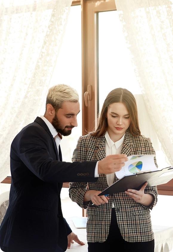 Man and woman in business attire reviewing documents with charts in a bright office setting.