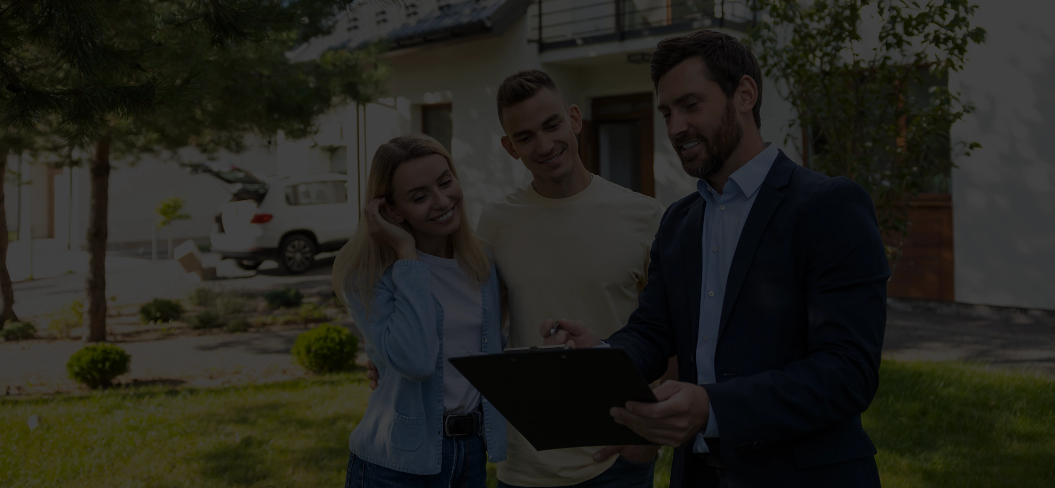 Real estate agent showing a clipboard and discussing with a smiling couple standing outside a house.
