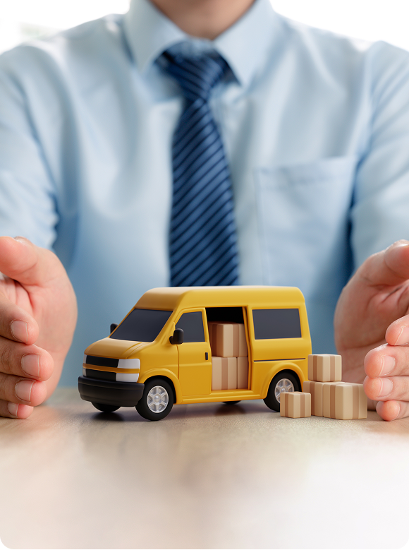 Person in blue shirt and striped tie protecting a yellow delivery van toy loaded with boxes on a table.