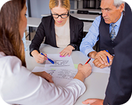 Four diverse business professionals sitting around a table reviewing and discussing documents together.
