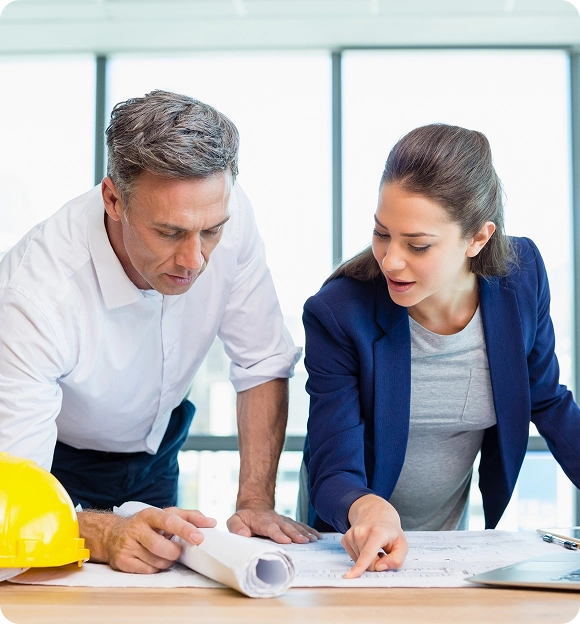 Two professionals discussing architectural plans on a table near a yellow safety helmet.
